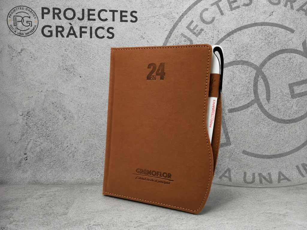 Agenda personalizada marrón con bolígrafo corporativo sobre fondo de Projectes Gràfics.