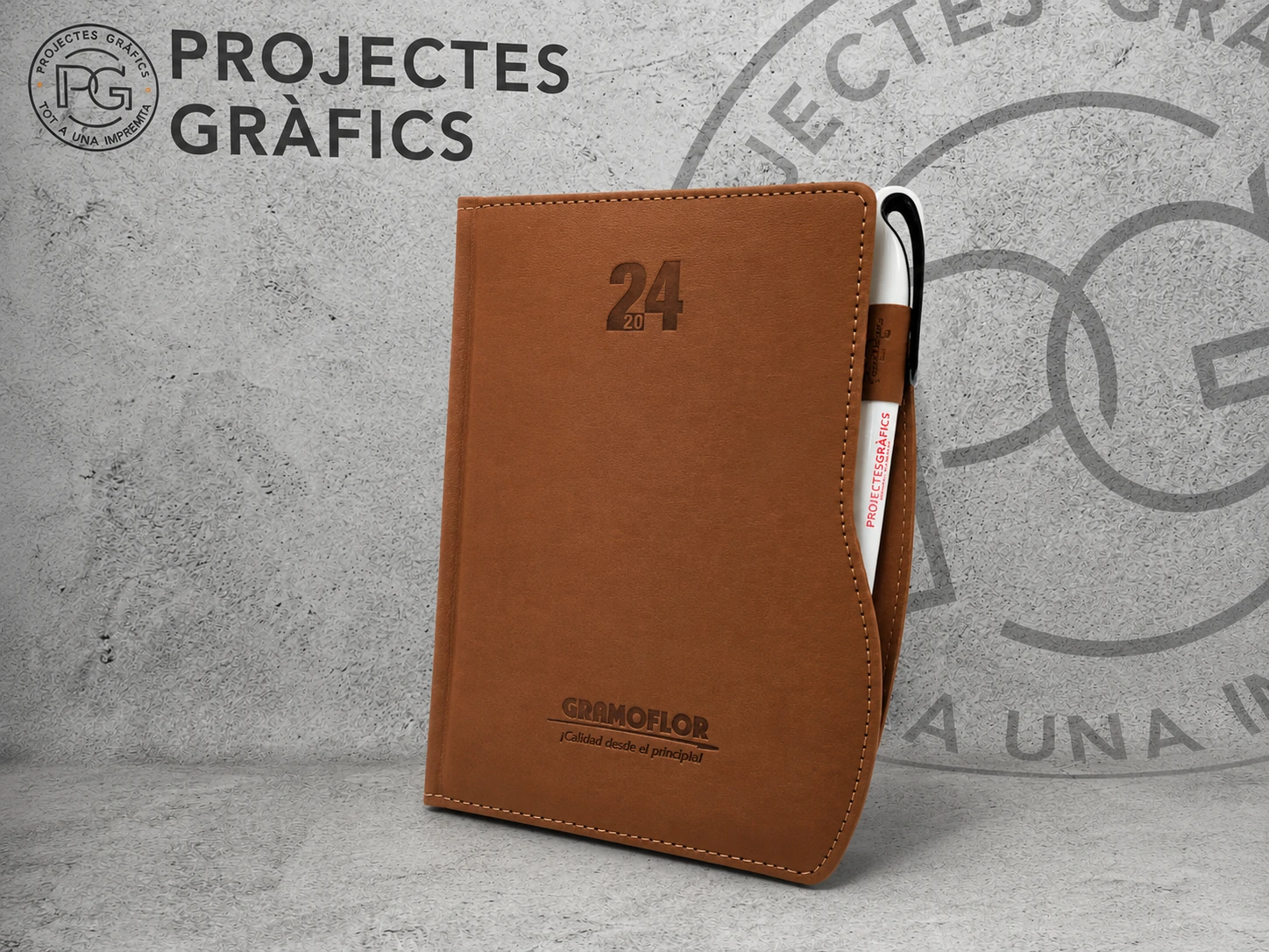Agenda personalizada marrón con bolígrafo corporativo sobre fondo de Projectes Gràfics.